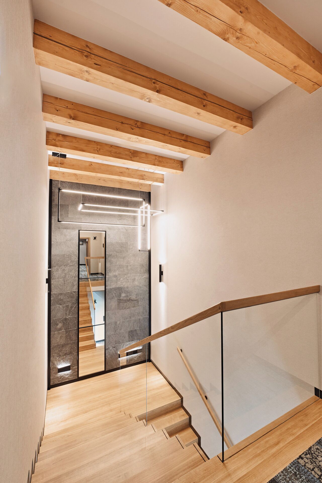 A modern interior with wooden beams, a glass railing, and a staircase leading to another room.