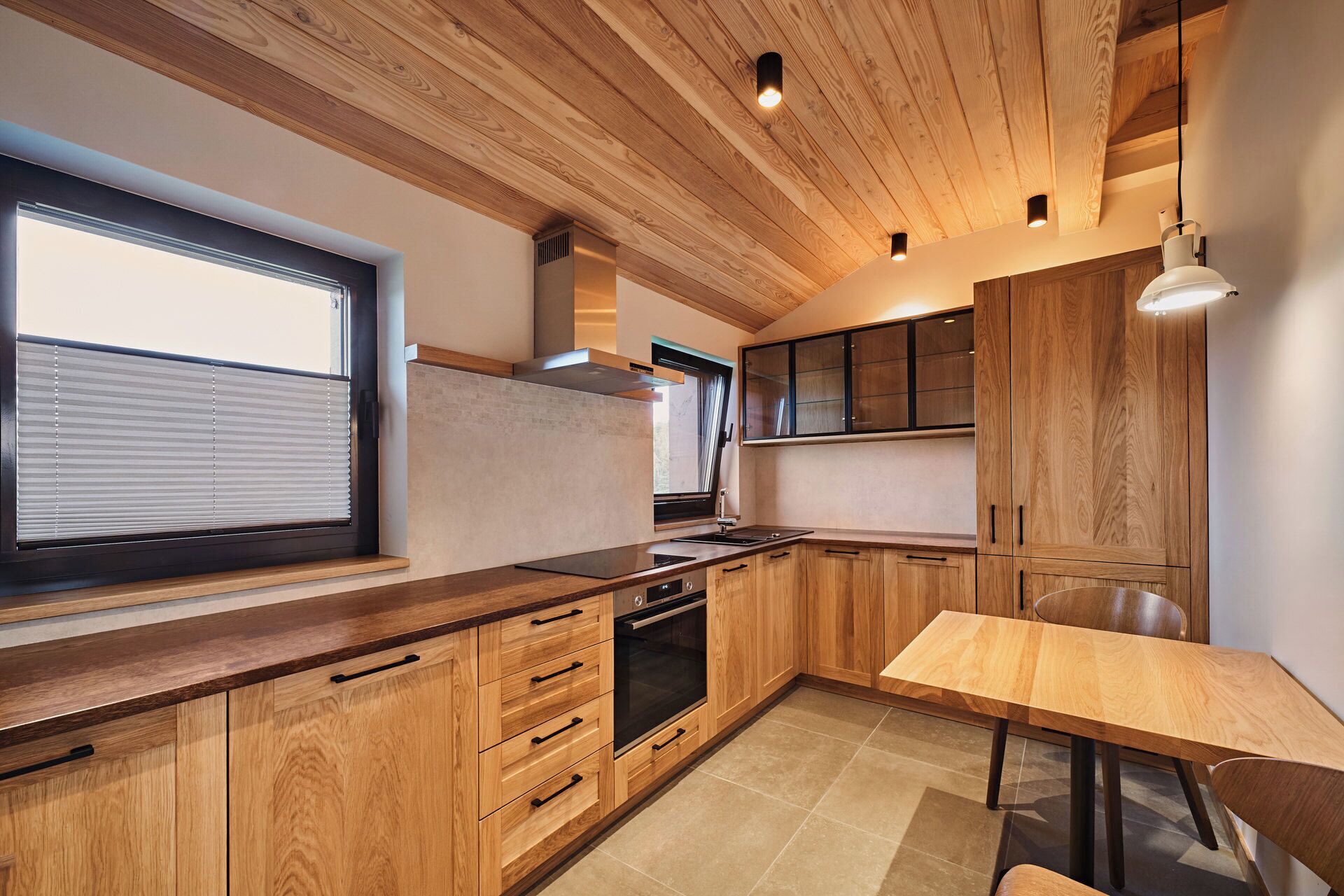 A modern kitchen with wooden cabinets, a built-in oven, and a window with blinds.