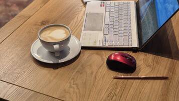 A wooden table with a laptop, a red mouse, a notebook, a pen, and a cup of coffee.