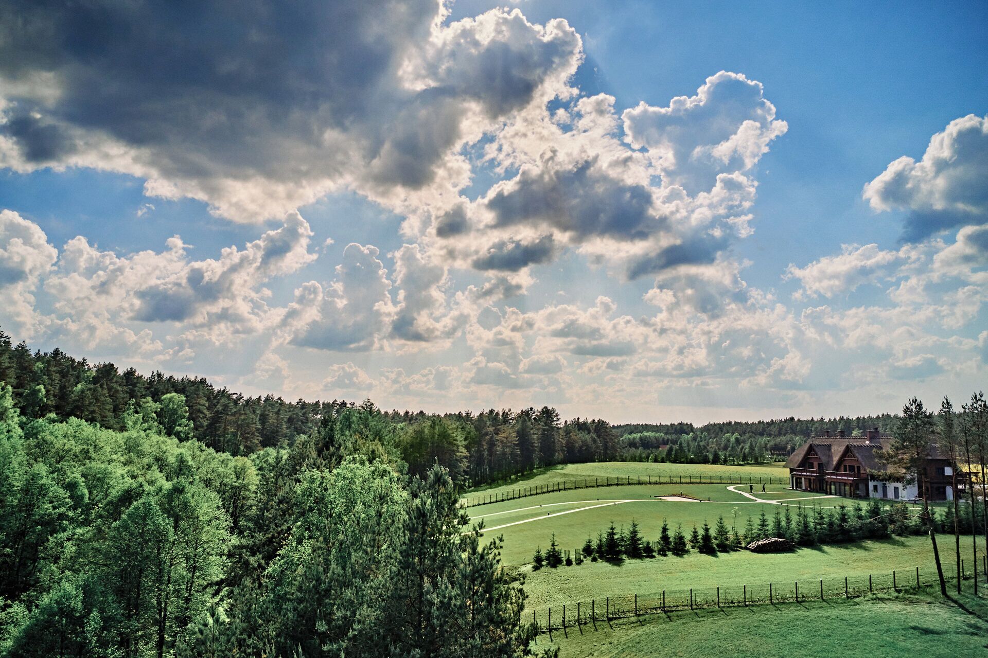 Een landelijk landschap met een huis, omringd door een omheind veld en dicht bos.