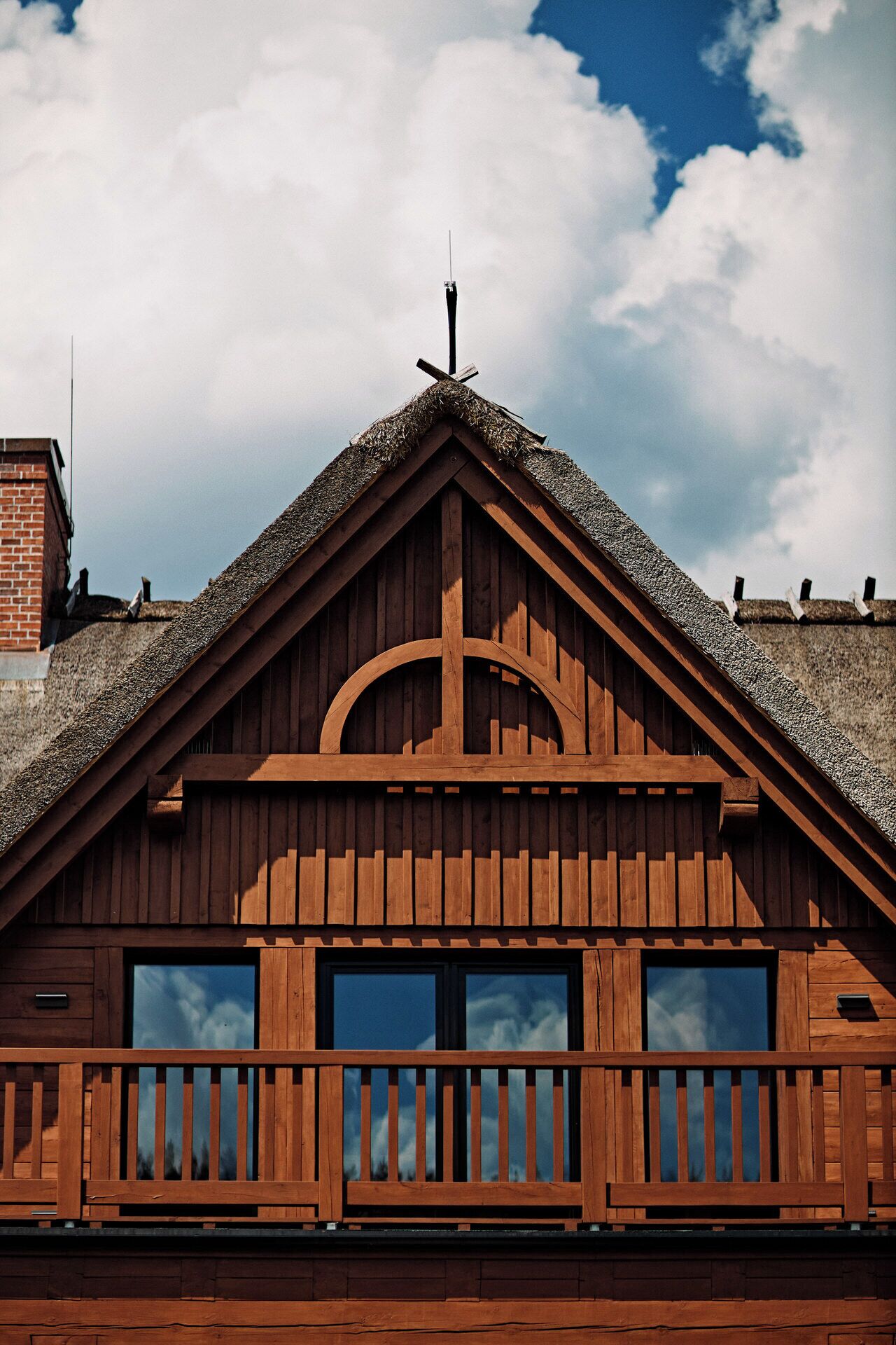 A wooden chalet with a steeply pitched roof, a balcony with wooden railings, and two large windows.