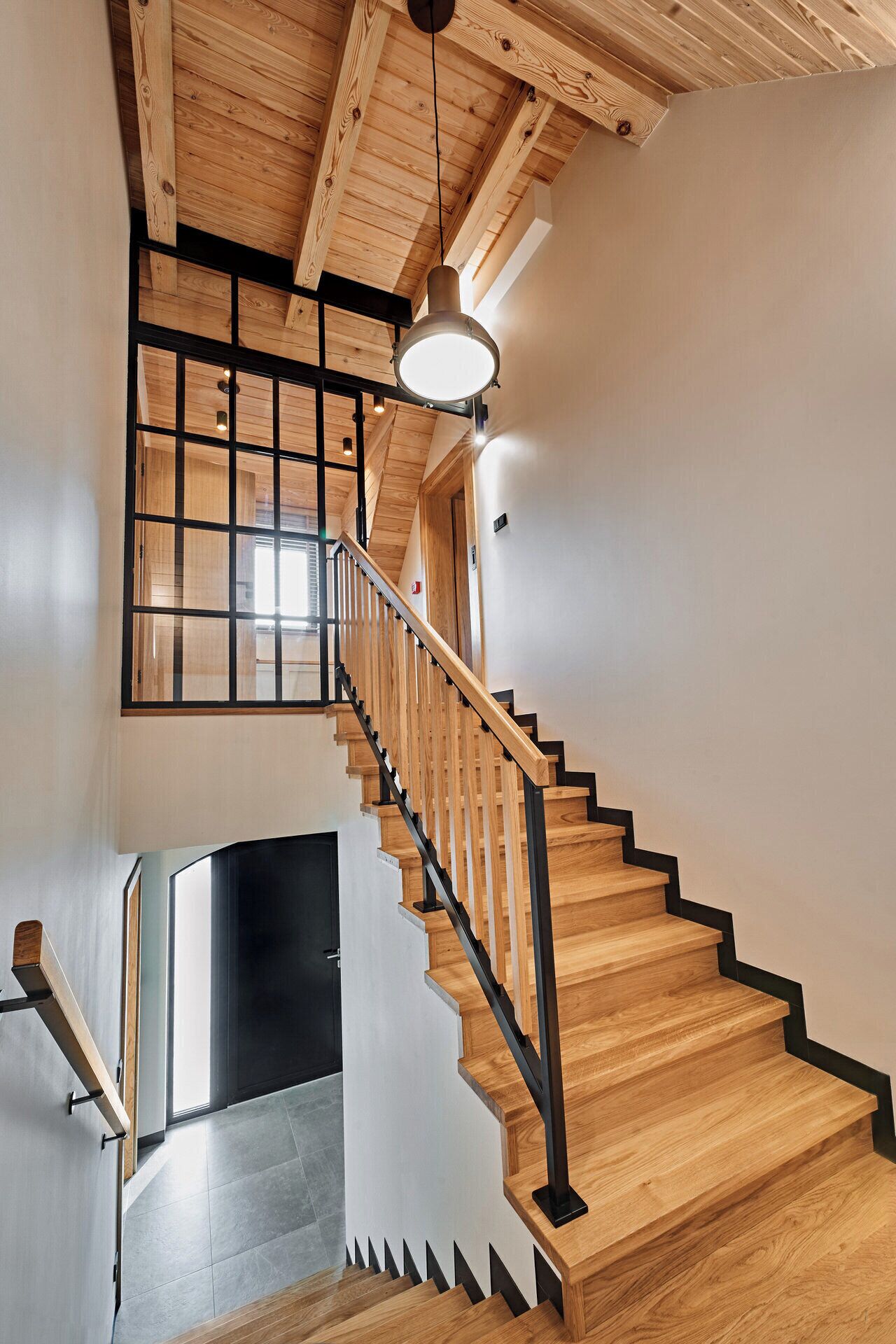 A wooden staircase with black railings and a hanging light fixture.