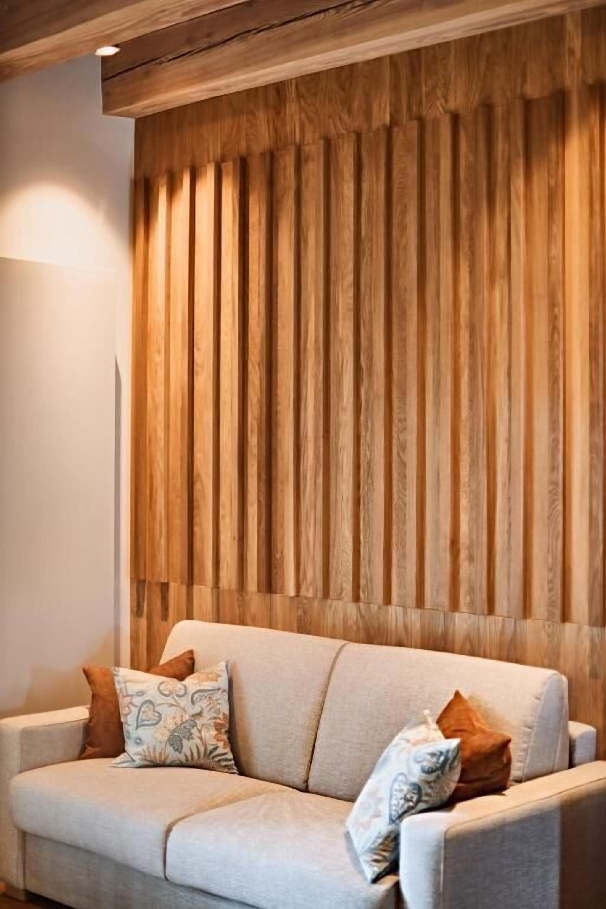 A modern living room with a light-colored sofa, two patterned throw pillows, and a wooden slat wall.
