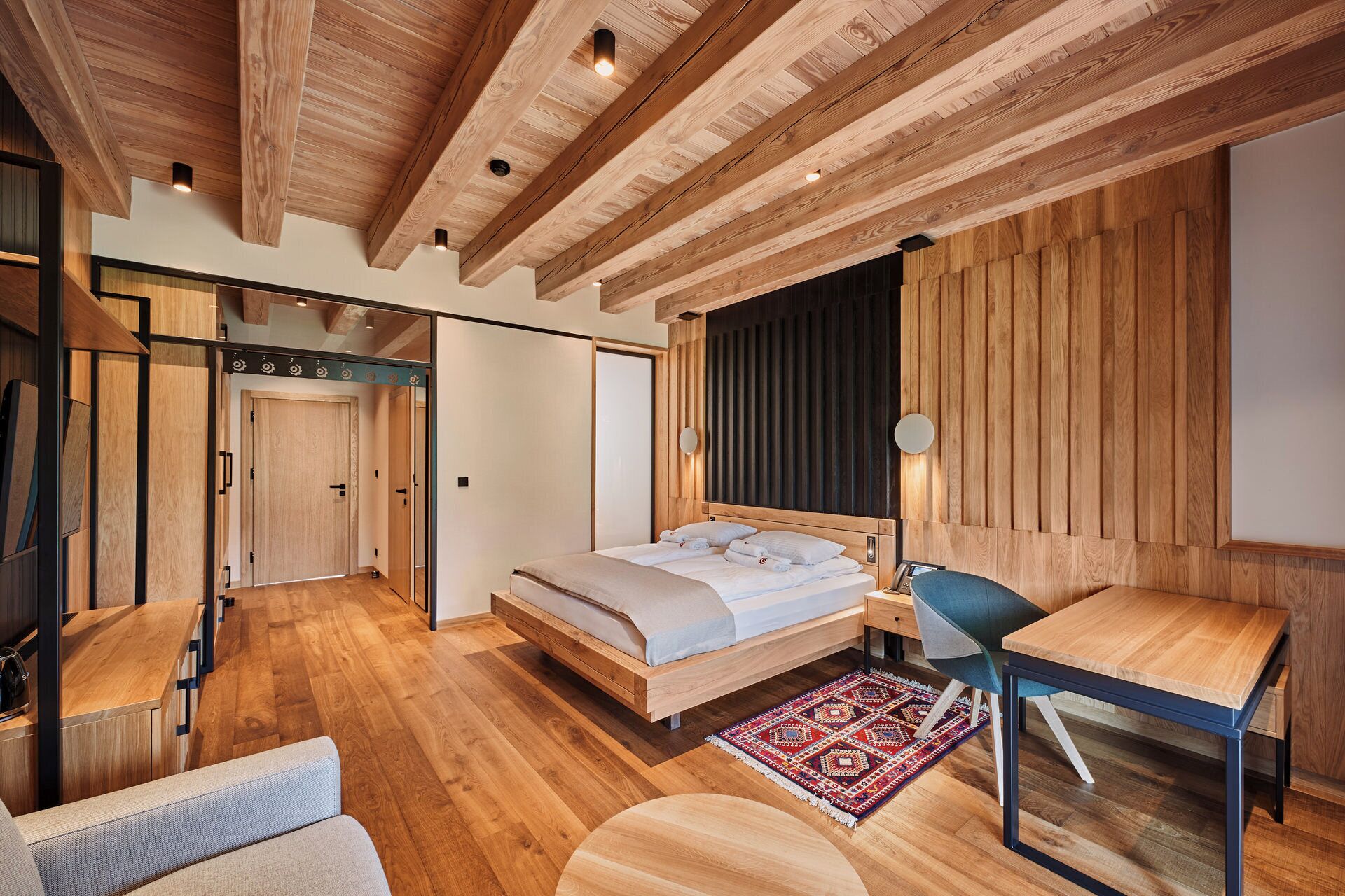 Un dormitorio moderno con techo de madera, una cama, un escritorio y una silla.