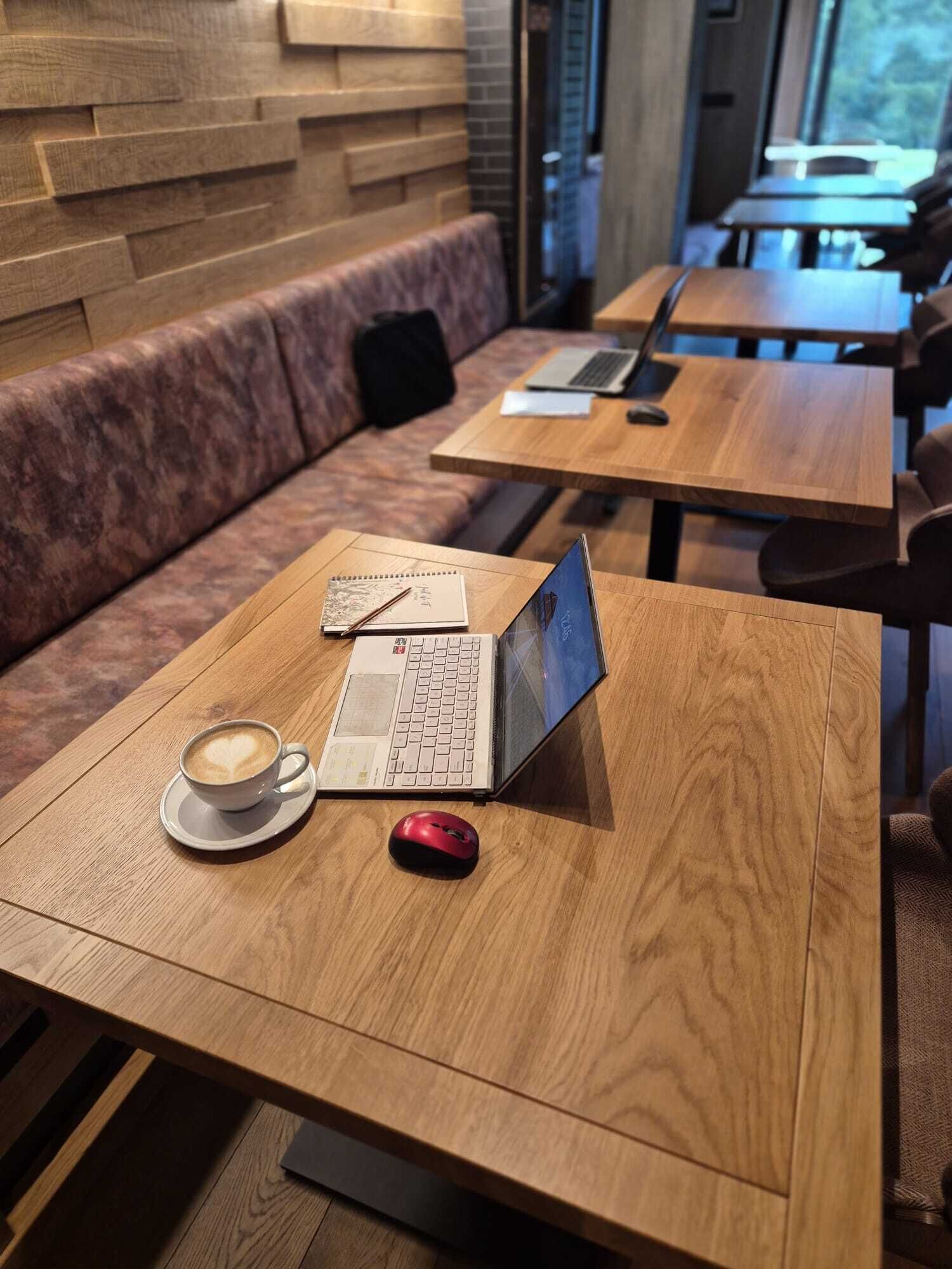A café with wooden tables, a laptop, a red mouse, and a cup of coffee on one table.