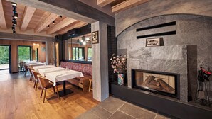 A dining area with wooden tables and chairs, a fireplace, and a view of the outdoors. - Siedlisko Milachowo luxury wellness (Brusy)