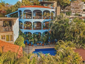 A two-story building with balconies, surrounded by lush greenery and a swimming pool. - Casa Del Morro - Studio Oasis with heated pool (Sayulita)