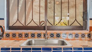 A kitchen with a stainless steel sink, a window with metal bars, and decorative tiles. - Casa Del Morro - Studio Oasis with heated pool (Sayulita)