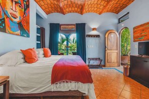 A bedroom with a bed, a TV, a wooden door, and a window with curtains. - Casa Del Morro - Studio Oasis with heated pool (Sayulita)