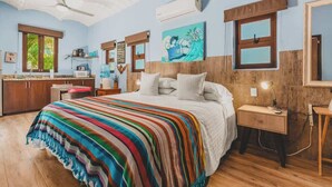 Un dormitorio con una cama grande, cabecera de madera, mesita de noche con lámpara, cómoda y ventana con vistas a zonas verdes.