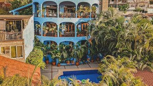 Un edificio de varios pisos con balcones, rodeado de exuberante vegetación tropical y una piscina.