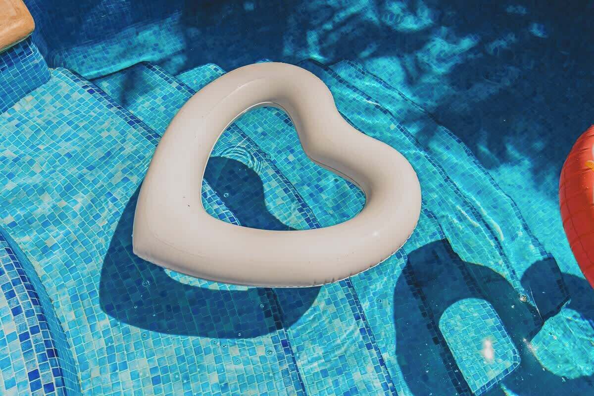 Un flotador con forma de corazón en una piscina con mosaicos azules.