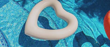 Un flotador con forma de corazón en una piscina con mosaicos azules.