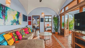 A spacious living room with a sofa, TV, and a large painting on the wall.
