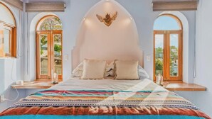 A bedroom with a large bed, a decorative ceiling, and windows with a view.