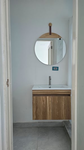 A bathroom with a round mirror, a white sink, wooden cabinets, and a tiled floor. - MR1-4 APARTAMENTO CON VISTA Y PISCINA (Cartagena)