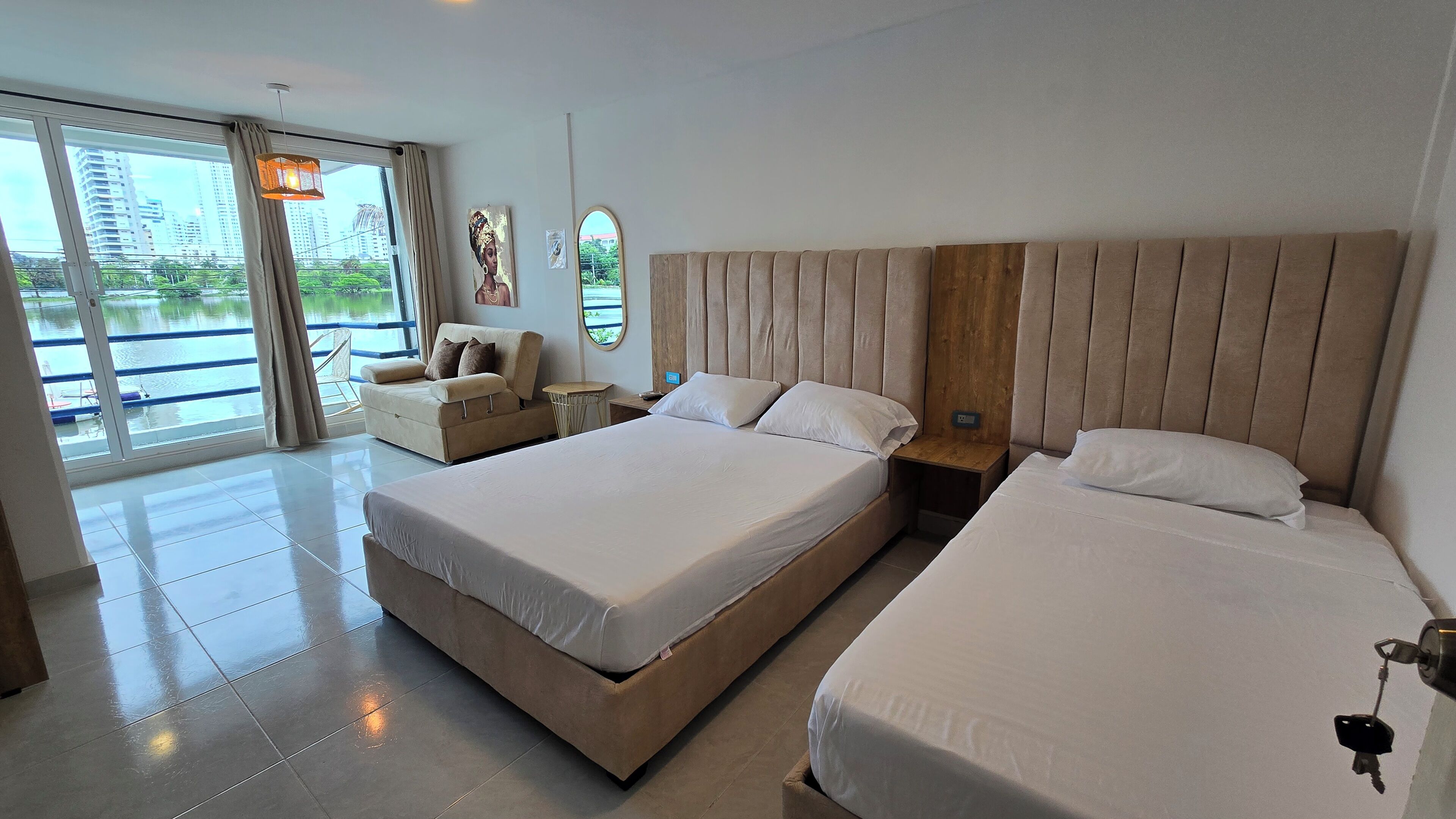 A hotel room with two beds, a sofa, a view of a body of water, and a balcony.