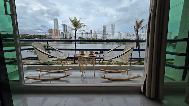 En balkon med to gyngestole og et lille bord, med udsigt over vand og bybillede.