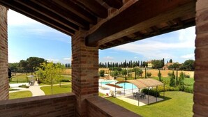 Vistes des d'un balcó de maó a una piscina, un porxo cobert i un jardí paisatjistic amb arbres i un edifici a la distància.