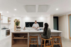 A modern kitchen with a central island, wooden stools, and a large window.