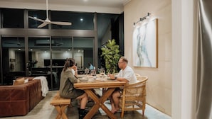 Een eetgedeelte met een tafel gedekt voor twee personen, een rieten stoel en een grote plant op de achtergrond.