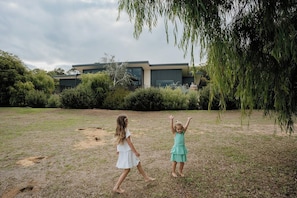 Dos niños jugando en un césped, con un edificio moderno al fondo.