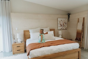 A bedroom with a wooden bed, white bedding, a nightstand, a lamp, and a painting on the wall.
