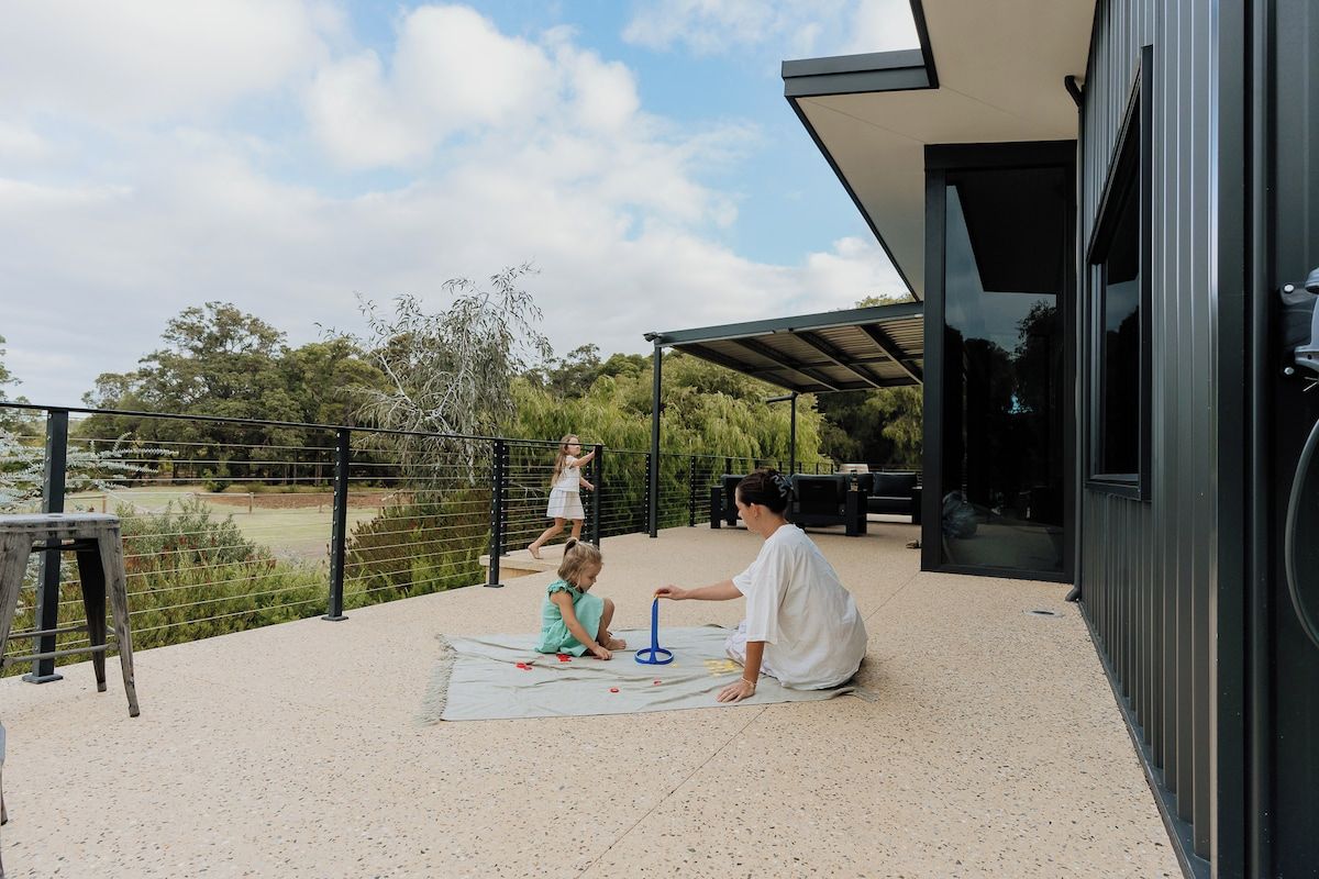 Un espace extérieur aménagé en patio, avec une clôture en métal, une table et une personne assise sur un tapis.