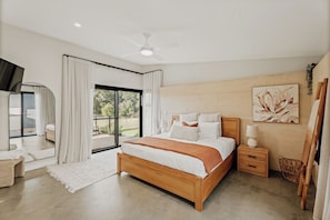 A modern bedroom with a large bed, a ceiling fan, a nightstand, and a view through a sliding glass door. - Wildwood—Luxe Vineyard Retreat with Tranquil Views (Yallingup Siding)