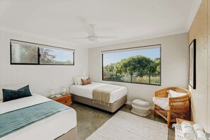 A bedroom with a bed, a chair, a bedside table, a window with a view of greenery, and a ceiling fan.