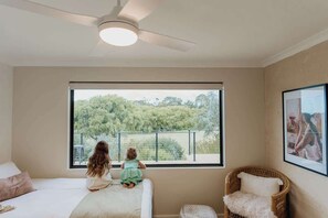 A bedroom with a large window, a bed, a chair, and a ceiling fan.