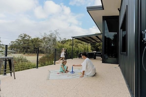 An outdoor patio with a metal fence, a child playing with a toy, and a person sitting on a mat.