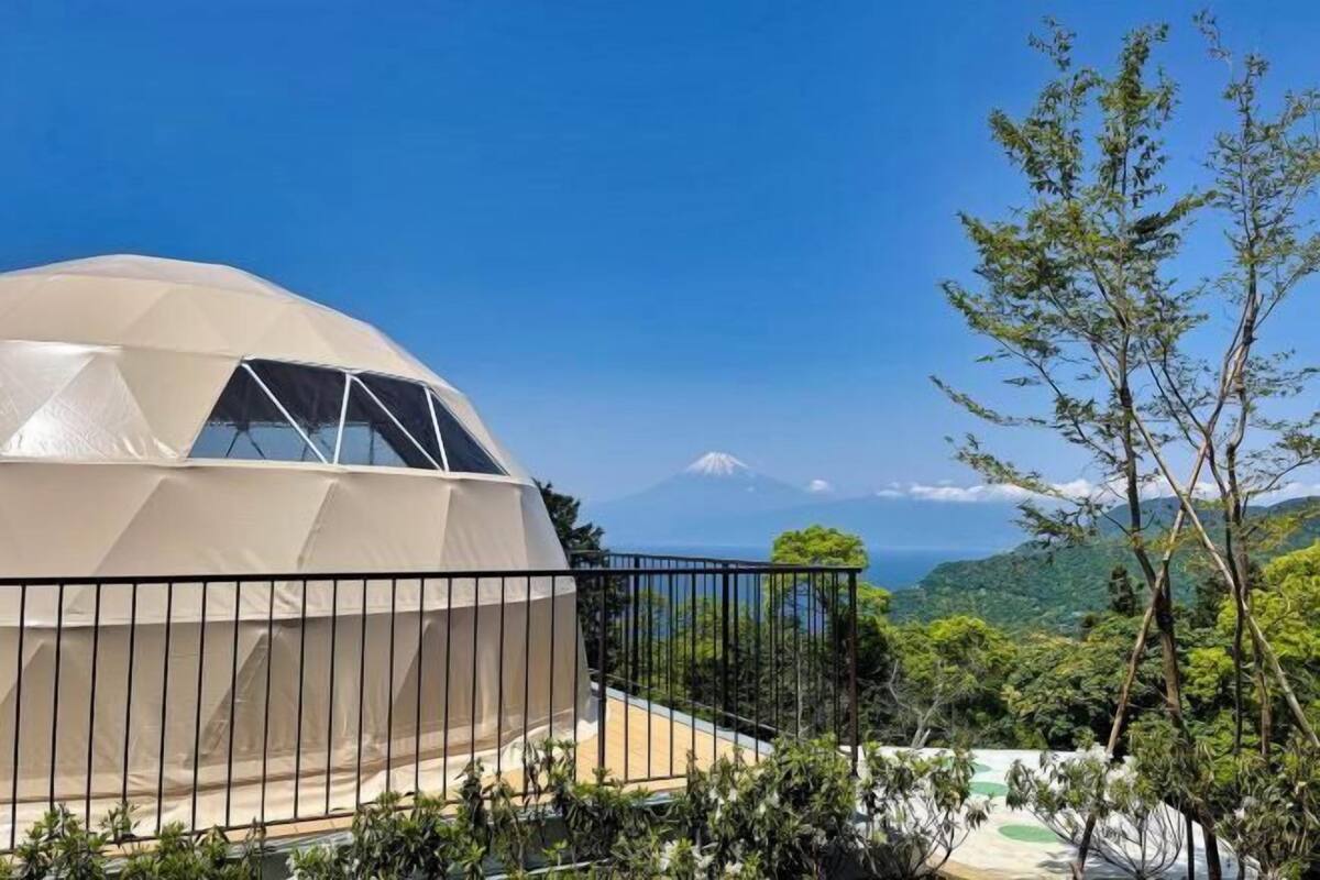 A dome-shaped building with a balcony, surrounded by lush greenery and a view of a distant mountain.