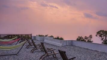 Une terrasse sur le toit, dotée de chaises longues et d’un hamac, offrant une vue sur le paysage urbain.