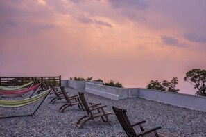 Een terras op het dak met lounge fauteuils en een hangmat, met uitzicht op een stadsbeeld.