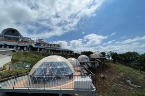A modern building with multiple dome-shaped structures, possibly for accommodation or events, with a clear sky in the background. - Nishi-izu Glamping Tenkuu-Terrace (Numazu)