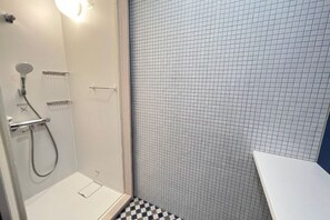 A shower with a handheld showerhead and a wall-mounted faucet, a tiled shower wall, and a white sink with a countertop. - Nishi-izu Glamping Tenkuu-Terrace (Numazu)