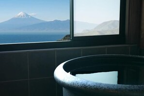 Baño con vista a una montaña y un cuerpo de agua a través de una ventana.