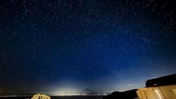 A starry night sky over a beach area with a few chairs and a building in the foreground. - Nishi-izu Glamping Tenkuu-Terrace (Numazu)