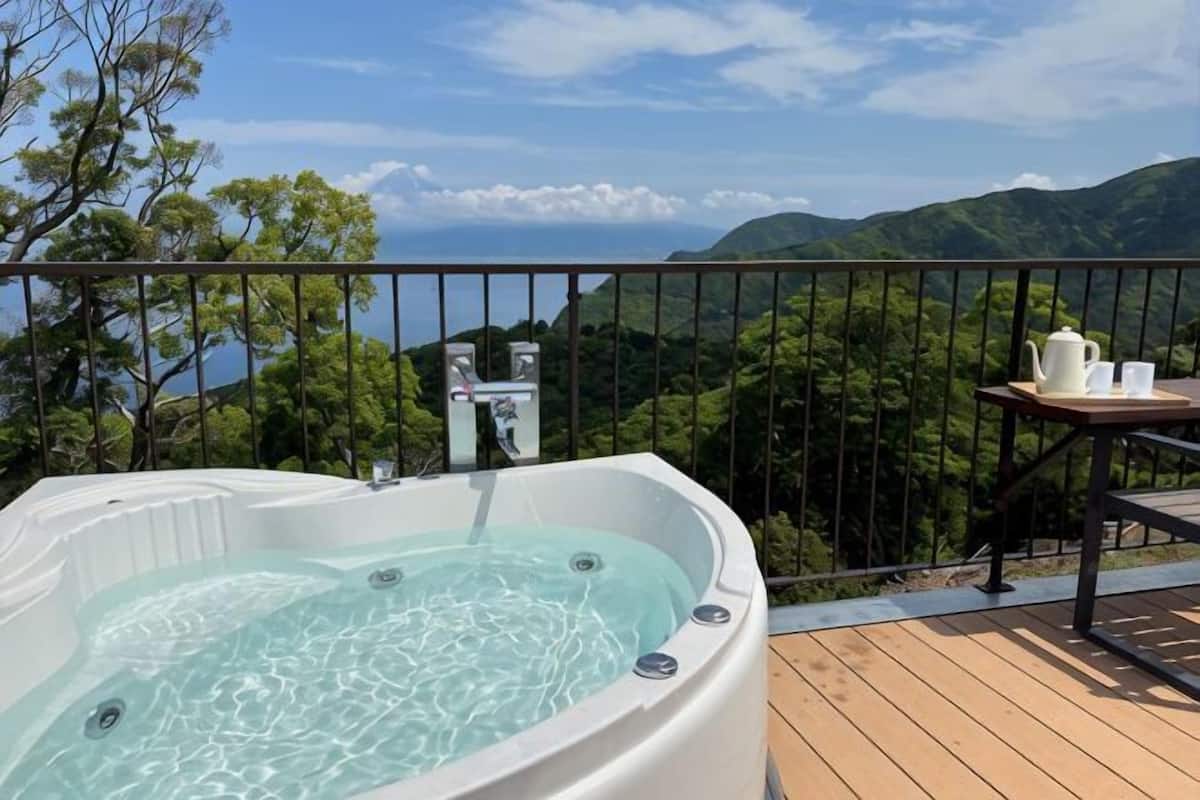 A hot tub on a wooden deck with a table and chairs, overlooking a mountainous landscape.