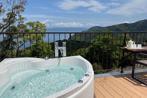 Un bain à remous sur une terrasse en bois, avec une table et des chaises, offrant une vue sur un paysage montagneux.