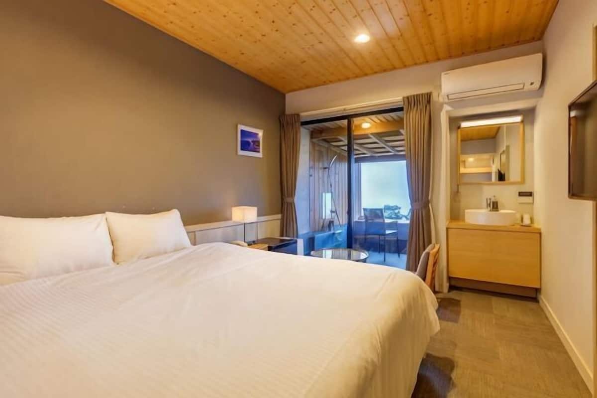 A hotel room with a large bed, a bathroom with a sink and mirror, and a balcony with a view.