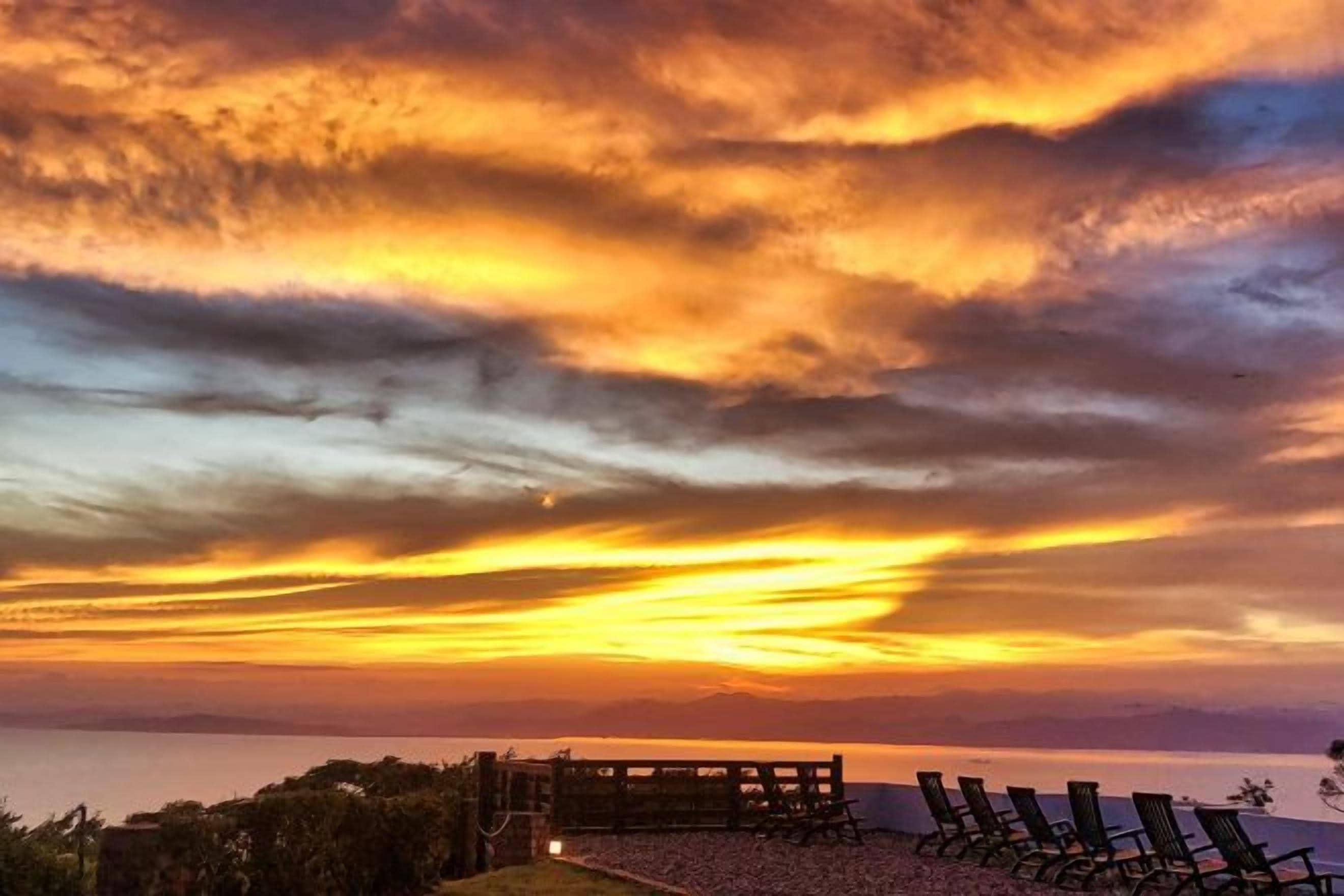 A sunset over a beach with a wooden pier and lounge chairs.