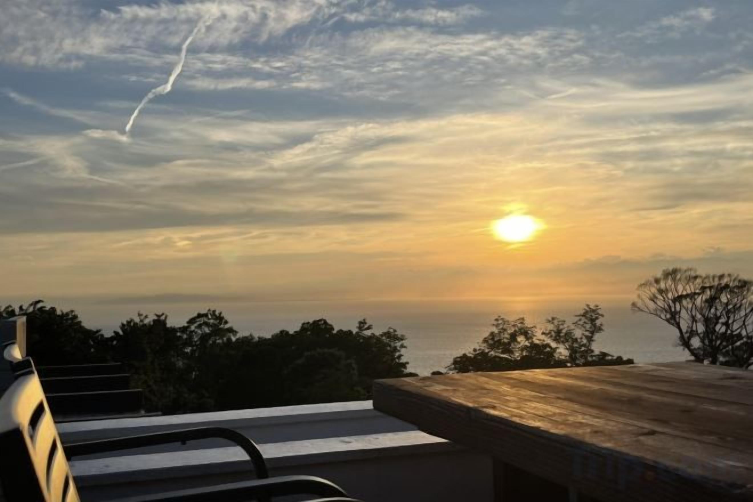 A sunset view from a balcony with a wooden railing and a bench.
