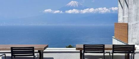 A terrace with tables and chairs overlooking a body of water and a mountain.