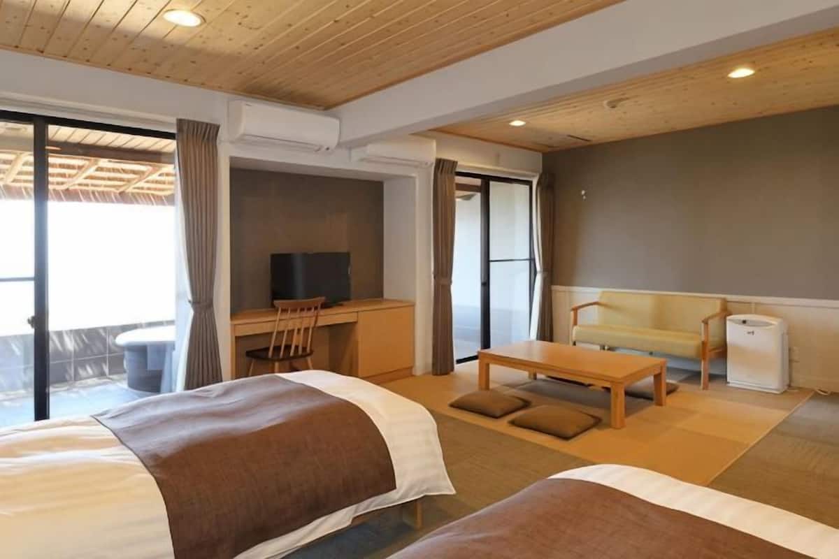 A hotel room with two beds, a desk with a TV, a sofa, and a small table.
