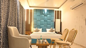 Une chambre d’hôtel avec un grand lit, deux fauteuils, une petite table avec une bouteille et un miroir.