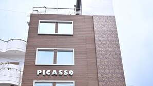Un bâtiment moderne avec une enseigne portant le mot « PICASSO », une voiture garée devant et un escalier menant à l’entrée.