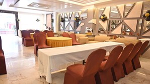 Une salle de banquet avec une longue table, des chaises à revêtement rouge et un sol en marbre.