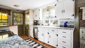 Une cuisine avec des meubles blancs, un plan de travail en marbre, un lave-vaisselle et une fenêtre donnant sur un espace verdoyant.